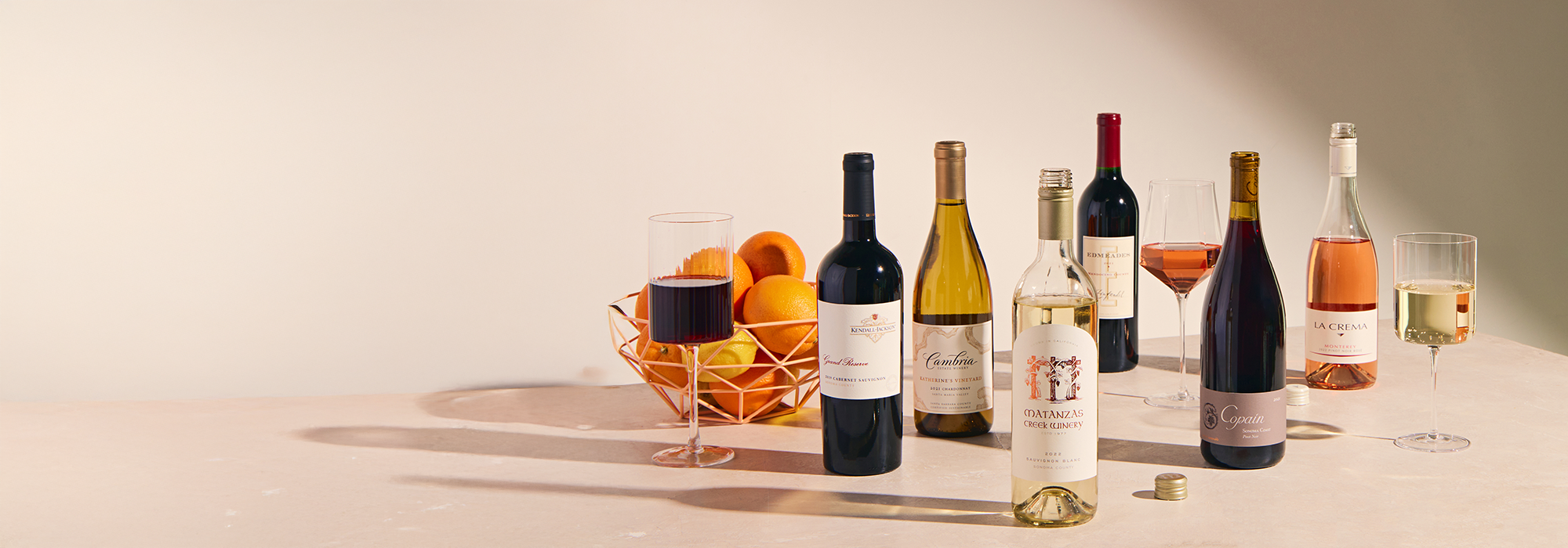 bottles of wine, wine glasses and a fruit basket filled with oranges
