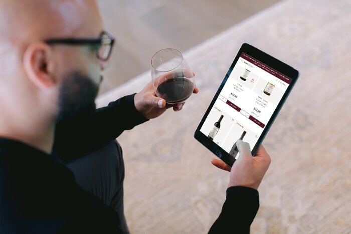 Person looking at tablet with glass of wine in hand.